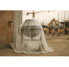 Bétonnière sur un chantier, recouverte d'une bâche de protection transparente, à côté d'une pelle et d'un mur en briques.