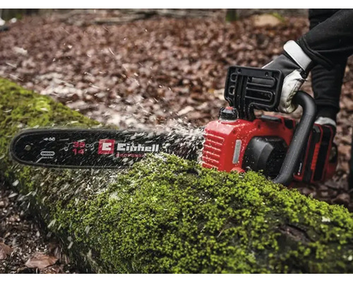 Tronçonneuse Einhell sciant un tronc couvert de mousse dans la forêt, copeaux de bois, longueur de guide 35 centimètres.