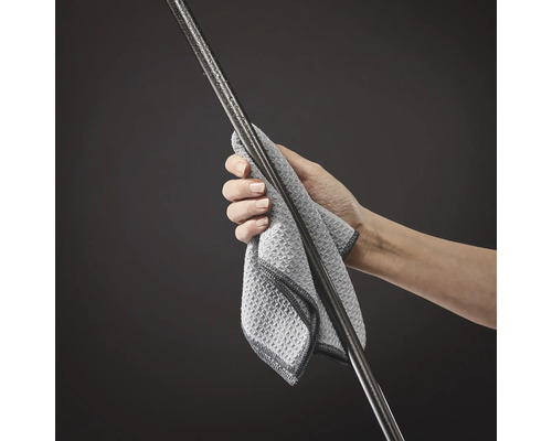 Eine Hand hält ein Mikrofasertuch und reinigt einen Metallstab mit Wassertropfen.