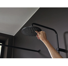 Eine Hand reinigt die Düsen eines runden Kopfbrause Modells in einer modernen Dusche mit dunklen Armaturen.