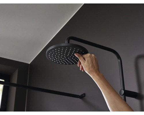Eine Hand reinigt die Düsen eines runden Kopfbrause Modells in einer modernen Dusche mit dunklen Armaturen.
