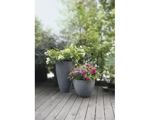 Zwei graue Pflanzkübel mit Rillenstruktur, bepflanzt mit Blumen auf einer Holzterrasse im Garten.