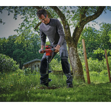 Un ouvrier utilise une tarière à batterie dans le jardin pour effectuer des travaux de terrassement dans la pelouse.