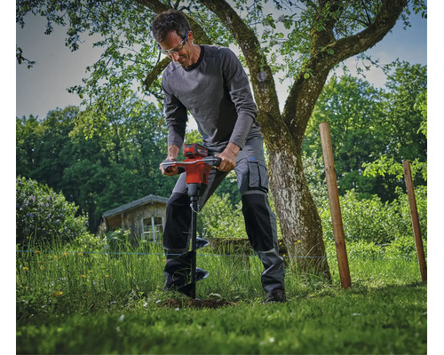 Un ouvrier utilise une tarière à batterie dans le jardin pour effectuer des travaux de terrassement dans la pelouse.