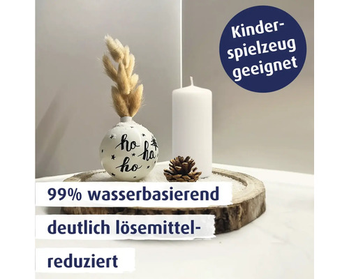 Weihnachtliche Tischdekoration mit einer bemalten Kugel, Stumpenkerze, Zapfen und getrockneten Gräsern auf einer Holzscheibe.