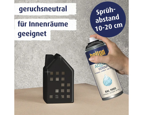 Hand hält eine Sprühdose Belton Aqua Colours zum Lackieren eines dekorativen Hauses, mit Hinweisen zu Geruchsneutralität und Sprühabstand.