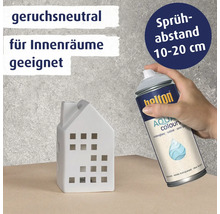 Eine Hand hält eine Belton Aqua Colours Klarlack Sprühdose zum Lackieren eines weißen Keramikhausmodells.