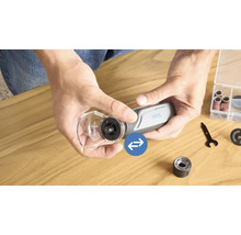 Personne monte un capot de protection sur un outil multifonction Dremel avec divers accessoires sur une table en bois.