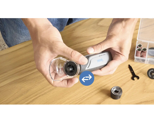 Personne monte un capot de protection sur un outil multifonction Dremel avec divers accessoires sur une table en bois.