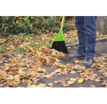Une personne balaie des feuilles mortes sur un chemin asphalté avec un balai de rue.