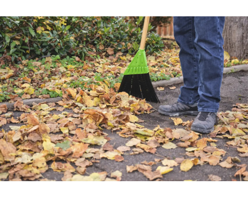 Une personne balaie des feuilles mortes sur un chemin asphalté avec un balai de rue.