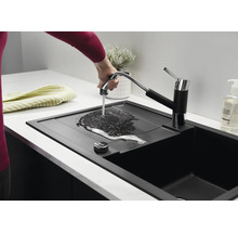 Un évier de cuisine noir moderne avec mitigeur extractible, où une main laisse couler de l'eau sur l'égouttoir.