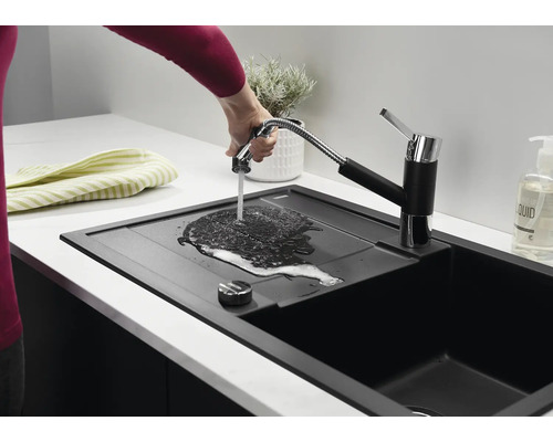 Un évier de cuisine noir moderne avec mitigeur extractible, où une main laisse couler de l'eau sur l'égouttoir.