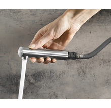 Main tenant une douchette extractible pour robinet de cuisine avec eau qui coule d un tuyau flexible.