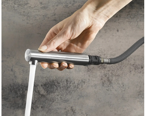 Main tenant une douchette extractible pour robinet de cuisine avec eau qui coule d un tuyau flexible.