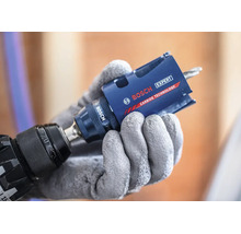 Eine Hand in Schutzhandschuh hält eine Bosch Expert Lochsäge mit Carbide Technologie an einem Bohrer.