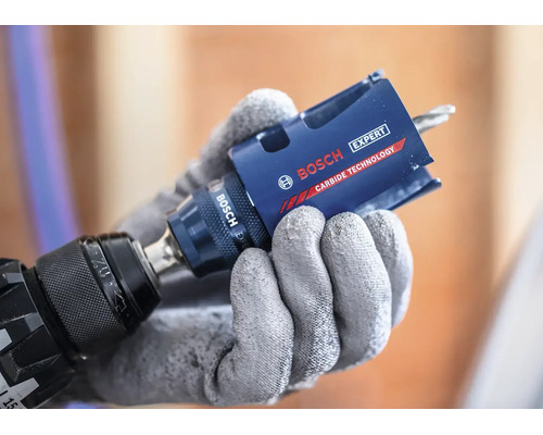 Eine Hand in Schutzhandschuh hält eine Bosch Expert Lochsäge mit Carbide Technologie an einem Bohrer.