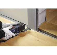 Un utilisateur portant des gants de travail utilise un outil multifonction Bosch pour couper un cadre de porte en bois afin d adapter un sol.