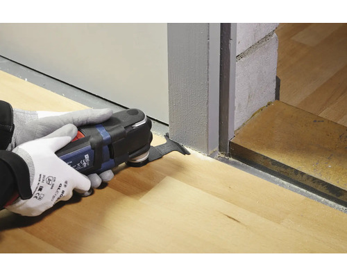 Un utilisateur portant des gants de travail utilise un outil multifonction Bosch pour couper un cadre de porte en bois afin d adapter un sol.