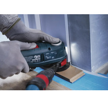 Une personne portant des gants de travail utilise un outil multifonction oscillant pour couper une plinthe.