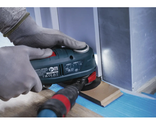 Une personne portant des gants de travail utilise un outil multifonction oscillant pour couper une plinthe.