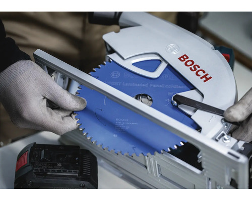 Une scie circulaire sans fil Bosch avec une lame de scie Expert Laminated Panel est montée par une personne portant des gants de travail.