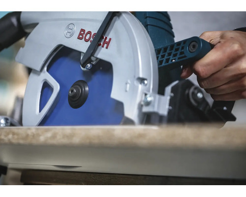 Une scie circulaire Bosch coupant une planche en bois, tenue par une main.