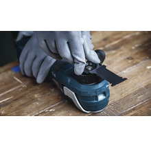 Une personne portant des gants de protection change la lame d une scie multifonction oscillante sur un établi.