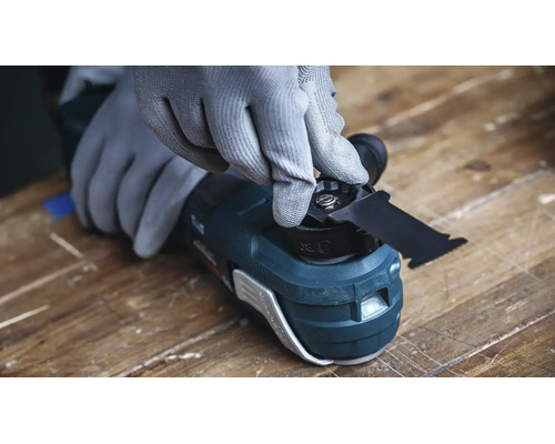 Une personne portant des gants de protection change la lame d une scie multifonction oscillante sur un établi.