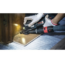 Un outil multifonction sans fil Bosch Professional en train de couper une pièce en bois avec un système d aspiration de poussière raccordé.