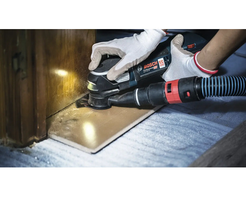 Un outil multifonction sans fil Bosch Professional en train de couper une pièce en bois avec un système d aspiration de poussière raccordé.