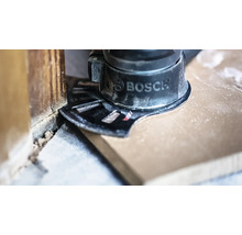 Outil multifonction Bosch avec lame de scie plongeante coupant un sol en bois à ras d'un mur.