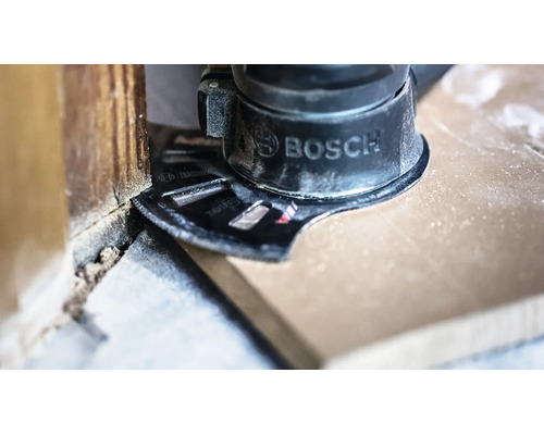 Outil multifonction Bosch avec lame de scie plongeante coupant un sol en bois à ras d'un mur.