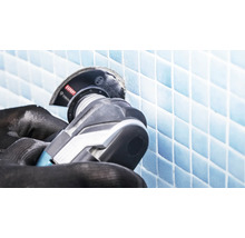 Une paire de mains gantées utilise un outil multifonction Bosch avec une lame diamantée pour couper des carreaux de mosaïque.
