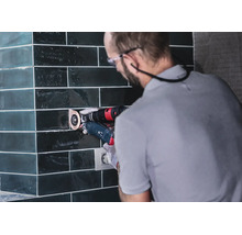 Artisan travaillant des carreaux avec un outil multifonction sur un mur carrelé