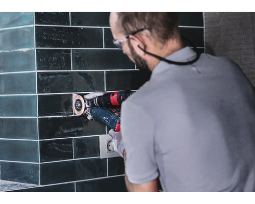 Artisan travaillant des carreaux avec un outil multifonction sur un mur carrelé