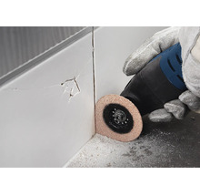 Meuleuse angulaire avec disque diamanté coupant un carreau mural fissuré.