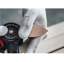 Person mit Handschuhen wechselt das dreieckige Schleifblatt an einem Multifunktionswerkzeug.