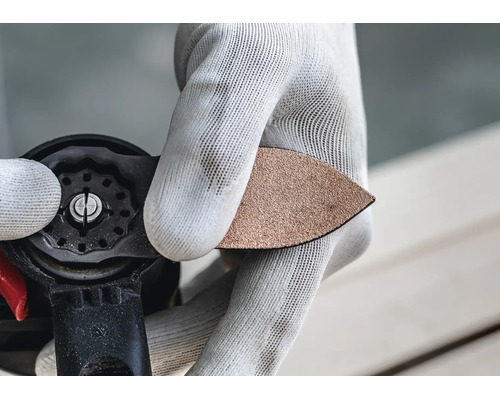 Person mit Handschuhen wechselt das dreieckige Schleifblatt an einem Multifunktionswerkzeug.