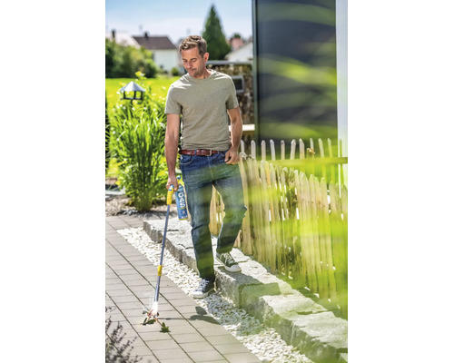 Ein Mann benutzt einen Gas Unkrautbrenner auf einer gepflasterten Gartenfläche, um Unkraut zwischen den Steinen zu entfernen.