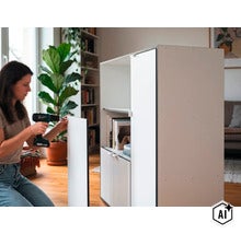 Une femme monte une armoire avec une perceuse sans fil dans un salon lumineux. (Image AI modified or generated)