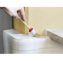 Eine Hand nutzt einen Rundpinsel, um eine Wand an einem Übergang zu einer weissen Leiste zu streichen.