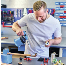 Un artisan brase un tuyau en cuivre avec un chalumeau dans un atelier.
