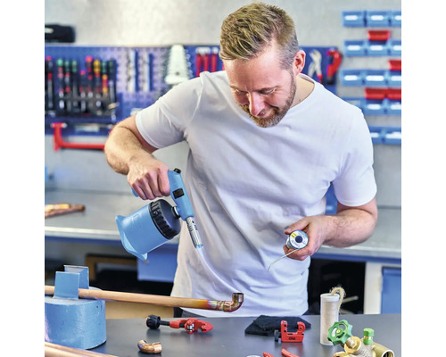 Un artisan brase un tuyau en cuivre avec un chalumeau dans un atelier.