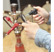 Une main allume du charbon à chicha avec un chalumeau à gaz, une chicha est posée sur une table en arrière-plan.