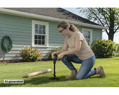 Une femme agenouillée sur une pelouse devant une maison utilise une tarière sans fil pour creuser un trou pour un poteau en bois.