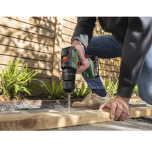 Une personne utilise une perceuse visseuse sans fil Bosch pour visser dans une planche en bois en extérieur.