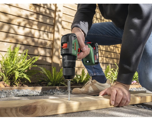Une personne utilise une perceuse visseuse sans fil Bosch pour visser dans une planche en bois en extérieur.