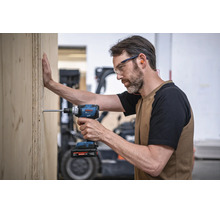 Artisan avec lunettes de protection utilisant une visseuse à chocs sans fil Bosch pour visser une plaque de bois dans un atelier.