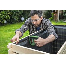Ein Handwerker nutzt einen Bosch Tacker zum Befestigen der Innenfolie an einem hölzernen Hochbeet im Garten.